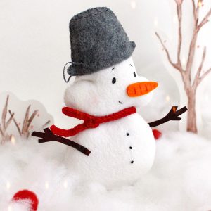 Felt toy Snowman with the pail on the head near the snow and drawing winter trees