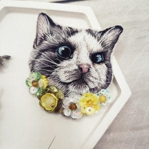 Brooch "Cat in flowers" is hand embroidered with threads, yellow flowers made of sequins and beads. Front view close up