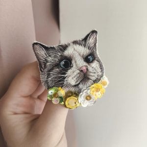 Brooch "Cat in flowers" hand embroidered with threads, yellow flowers made of sequins and beads. Front view, in hands, natural size